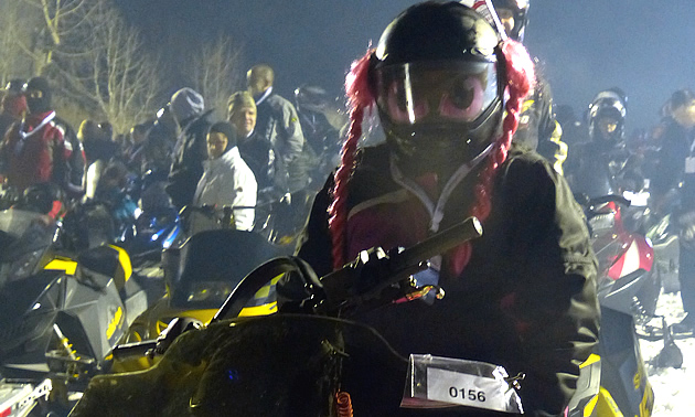 A woman with pink pigtails hanging from her snowmobile helmet. 