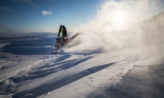 sillhouette of a snowmobiler with powder flying up