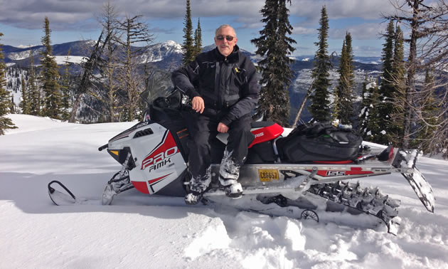 A grey-haired man sitting on his Pro-RMK snowmobile. 