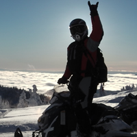 A silhouette of a woman standing on a snowmobile above the clouds. 