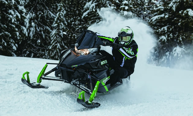 A guy cornering on a black and green sled. 