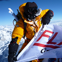 A climber holing the Flaman flag at the top of Mount Everest