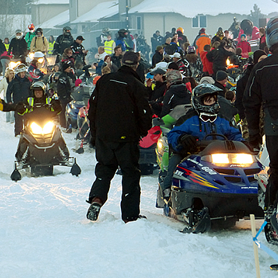 A large group of snowmobilers waiting for a ride to begin. 