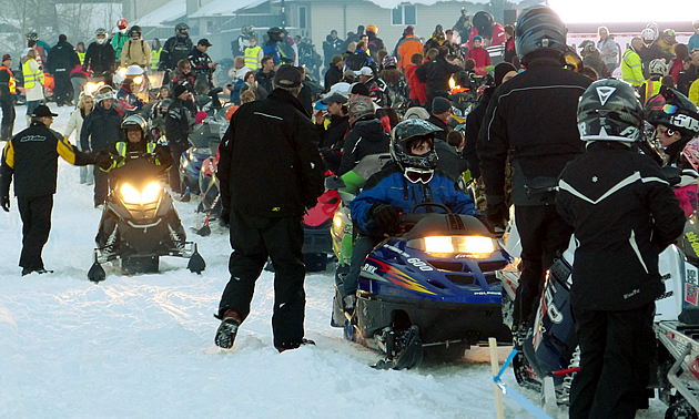 A large group of snowmobilers waiting for a ride to begin. 