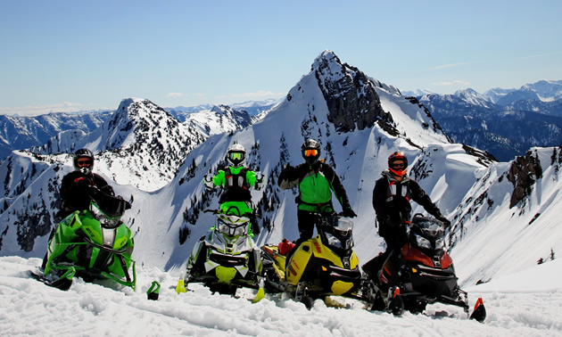 Four sledders parked on top of a mountain with the Rockies in the background. 