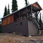 a cedar-sided cabin with a covered deck in the woods