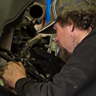 A brown haired man in a ball cap working on an engine. 