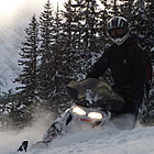 A guy wearing all black riding a white snowmobile on the trail.