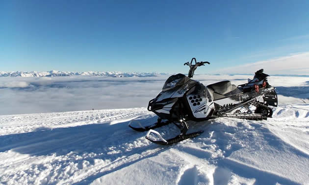 A Black and white Ski-Doo parked at the top of a mountain. 
