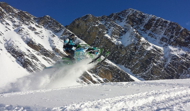 Heather White catching some air on her sled.  She has a range of mountains showing in the near background. 