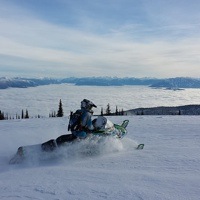 Heather White on her sled overlooking a vista of mountains peaking through the cloud cover. 