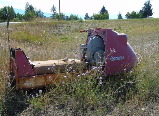 Another view of vintage Herters snowmobile sitting in tall grass. 
