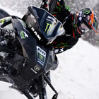 A guy in all black racing a black snowmobile.