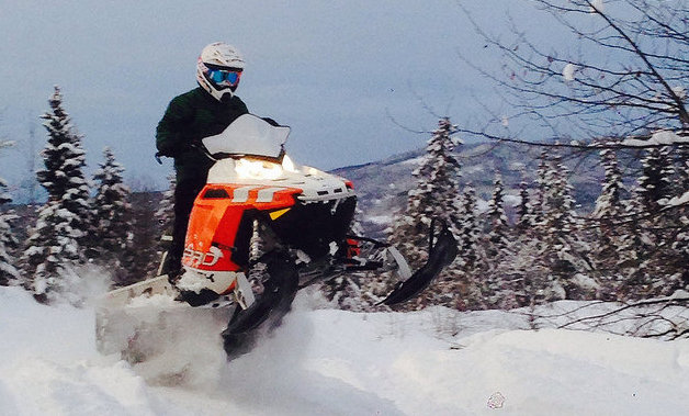A snowmobiler on an orange and white sled getting some air. 