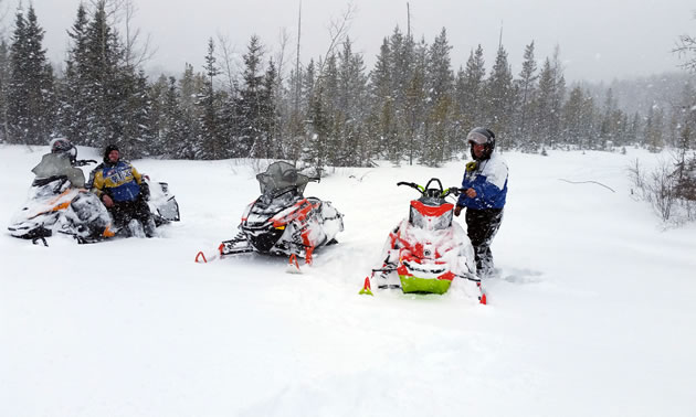 Three sleds and two riders stopped on the snowy trails in Hudson Bay. 