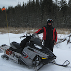 Man standing beside a snowmobile and a beaver lodge.