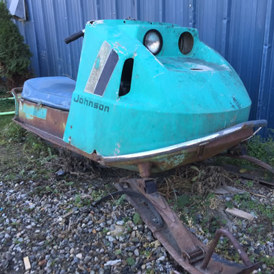 Picture of the front of a rusting Johnson snowmobile. The colour of the snowmobile is baby blue. 