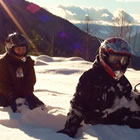 Photo of two young people sitting on the snow on top of a mountain.