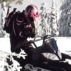A woman in a pink helmet on a black snowmobile in the backcountry. 