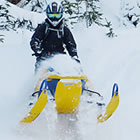 A person in black helmet and jacket on a blue and yellow Ski-Doo snowmobile. 