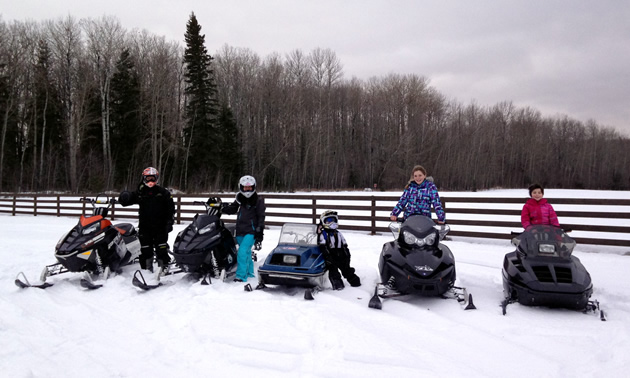 A mother and father with their three kids on snowmobiles. 