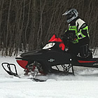 Photo of a woman riding a red and black snowmobile right next to a forest.