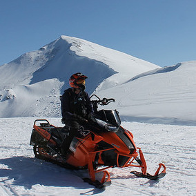 A sledder stopped with two mountain peaks in the background. 
