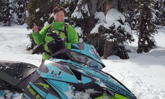 Melanie Tonsi beside her snowmobile giving a thumbs up