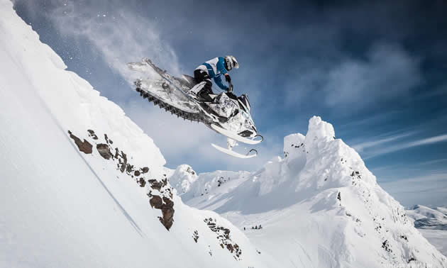 A man soaring through the air on a sled in the mountains of Finland.
