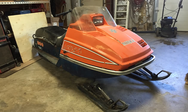 An orange Mirage snowmobile sitting inside of a garage. 