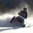 A snowmobiler in a black helmet on a black and white sled. 