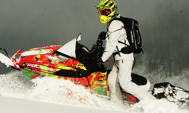 A woman in an all-white sledding outfit on an Pro-RMK. 