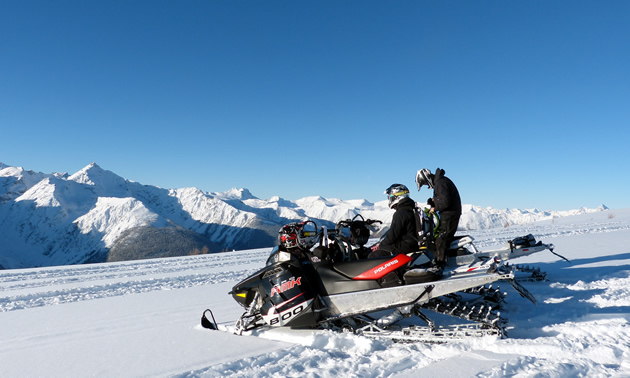 Mountain snowmobilers sitting on top of a mountain on a bluebird day. 