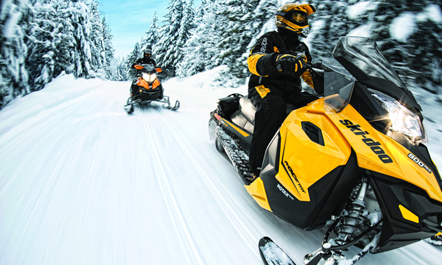 A person riding a yellow Ski-Doo on the trail.  