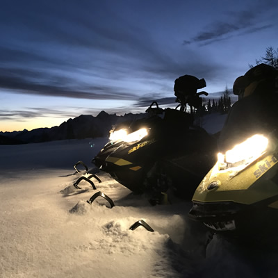 Three Ski-Doo's lined up on top of the mountain. 