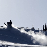An outline of a sledder jumping with powder spraying behind him. 