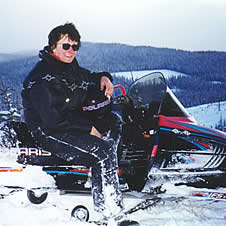 Profile shot of woman with snow-crusted legs sitting astride a snowmobile