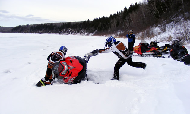 Snowmobilers trying to get a tipped over sled upright. 