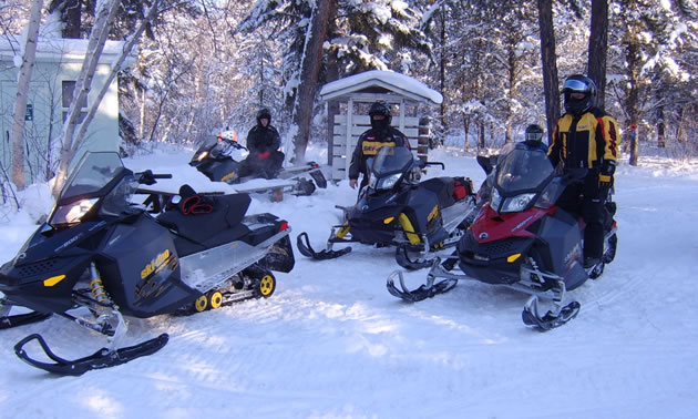 A group of snowmobilers standing by their sleds near a warm up shelter. 