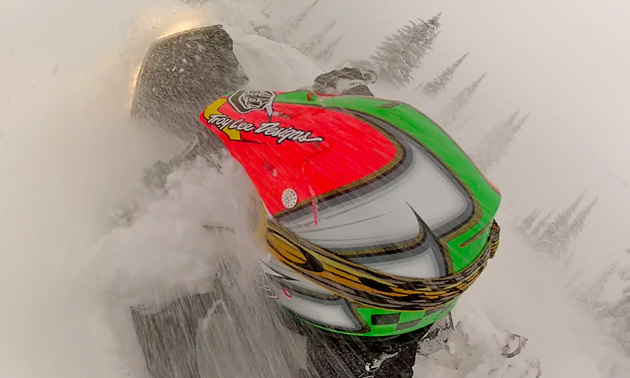 The back of a guys helmet while he is riding through the snow. 