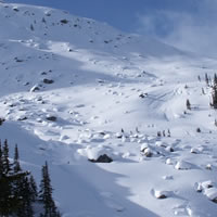 A slope with snow but rocks and trees are exposed. 