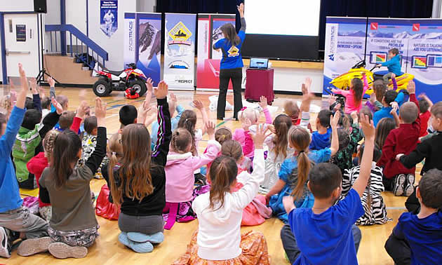 A group of children in a gym with their hands up. 