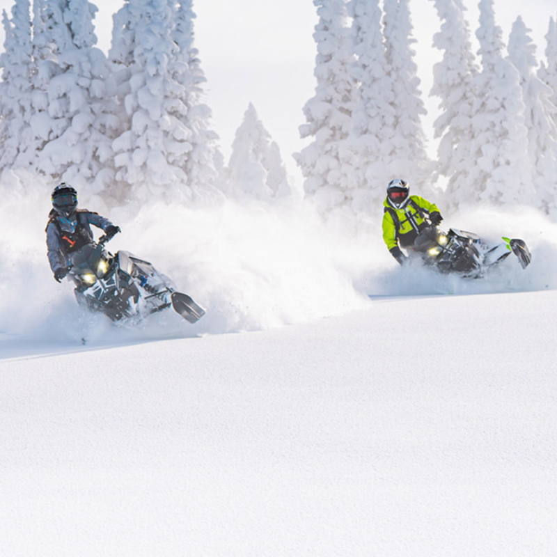 Two sleds being ridden in snow