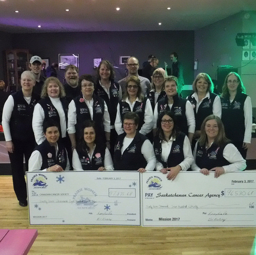 Volunteers with the Mission Ride of Prairie Women on Snowmobiles are lined up with two large imitation donation cheques in front of them.