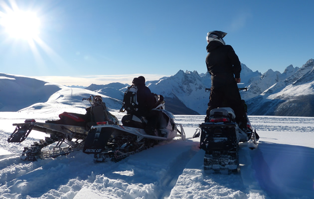 Two snowmobilers looking at mountains in the distance. 