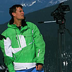 A man in a bright green jacket and a guy on a snowmobile looking to the mountains. 