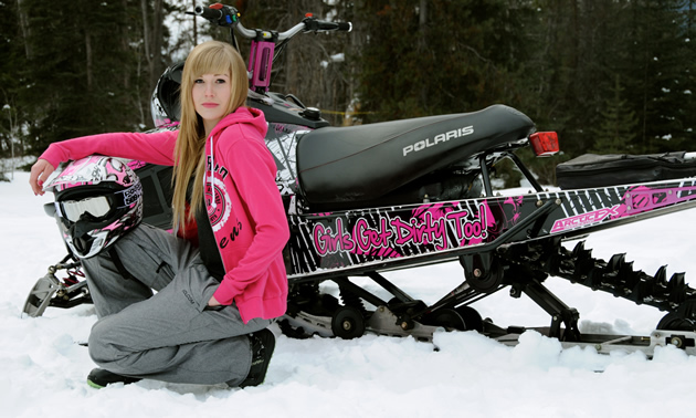 A young woman with long blonde hair sitting by a pink sled. 