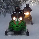 A person wearing black on a green sled with a person behind them on a yellow sled. 