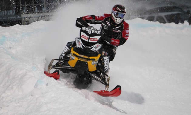 A guy on a black and yellow snowmobile racing. 