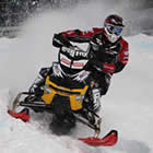 A guy on a black and yellow snowmobile racing. 